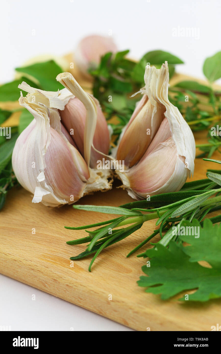 Closeup of garlic cloves and fresh herbs on wooden board Stock Photo