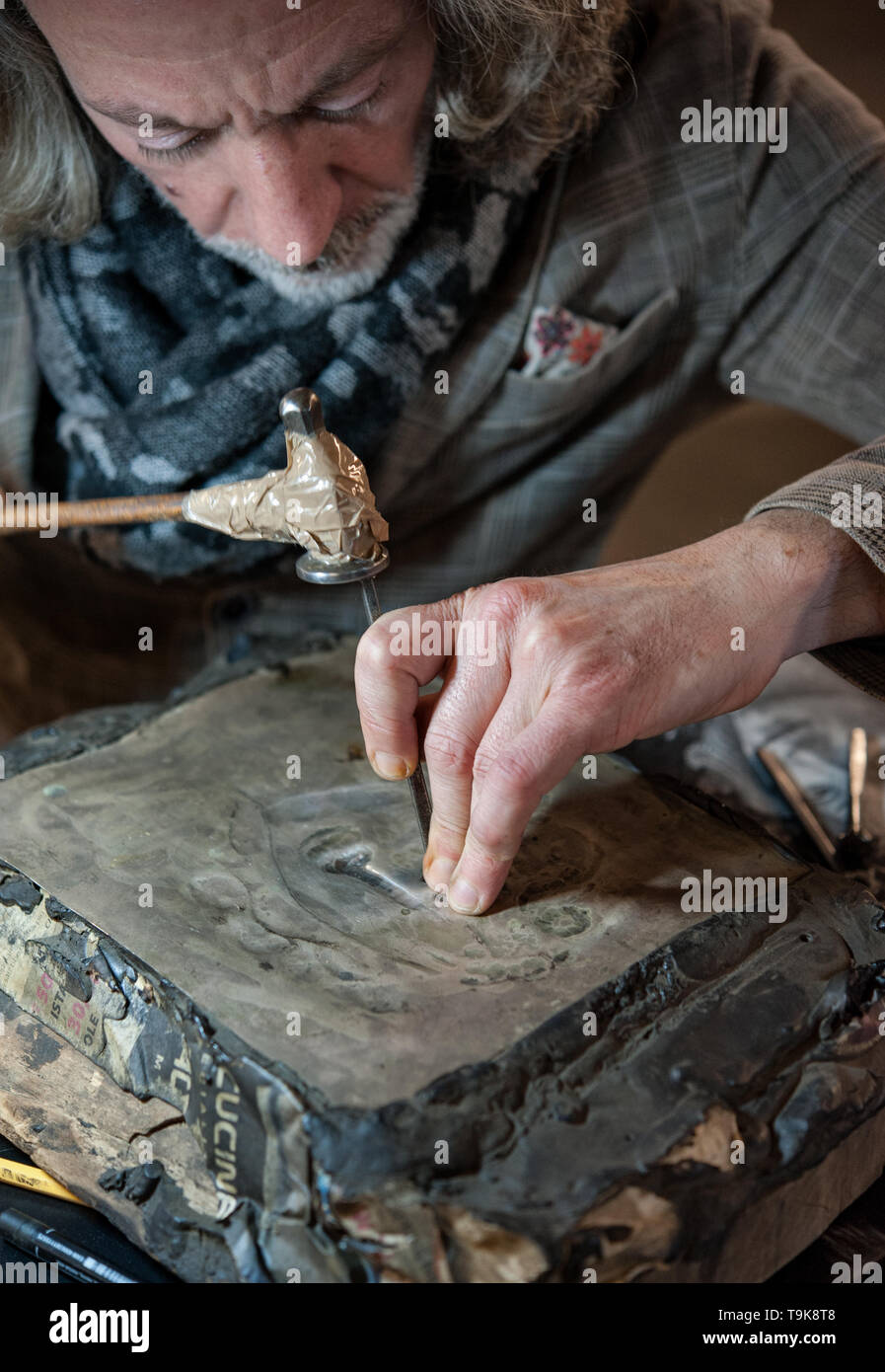 Master craftsman engraves a silver plate with hammer and chisel. Stock Photo