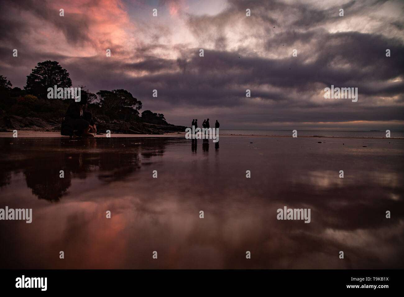 Beach reflection of the sunrise in Devonport Tasmania, young men standing around chatting Stock Photo