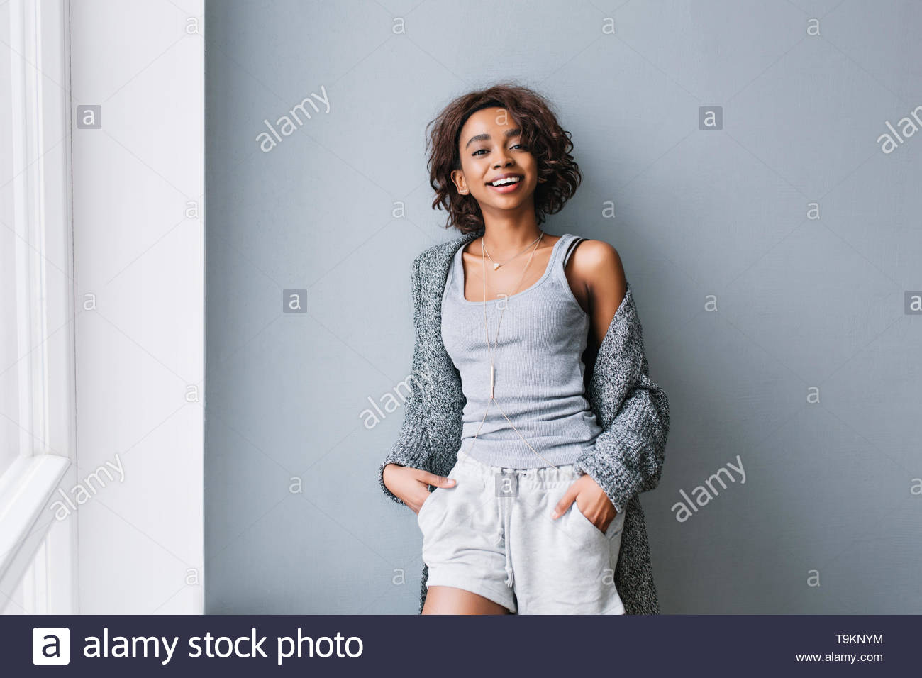Joyful Young Girl With Short Curly Hair Standing Next To Gray Wall