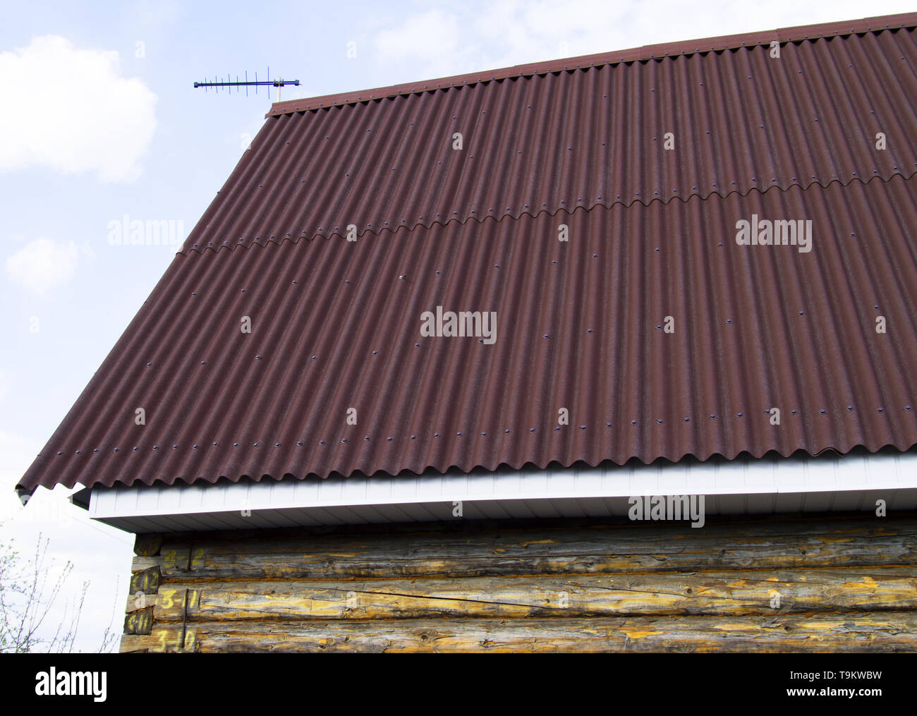 modern construction of the roof with red metal siding to a wooden house in the garden. Stock Photo