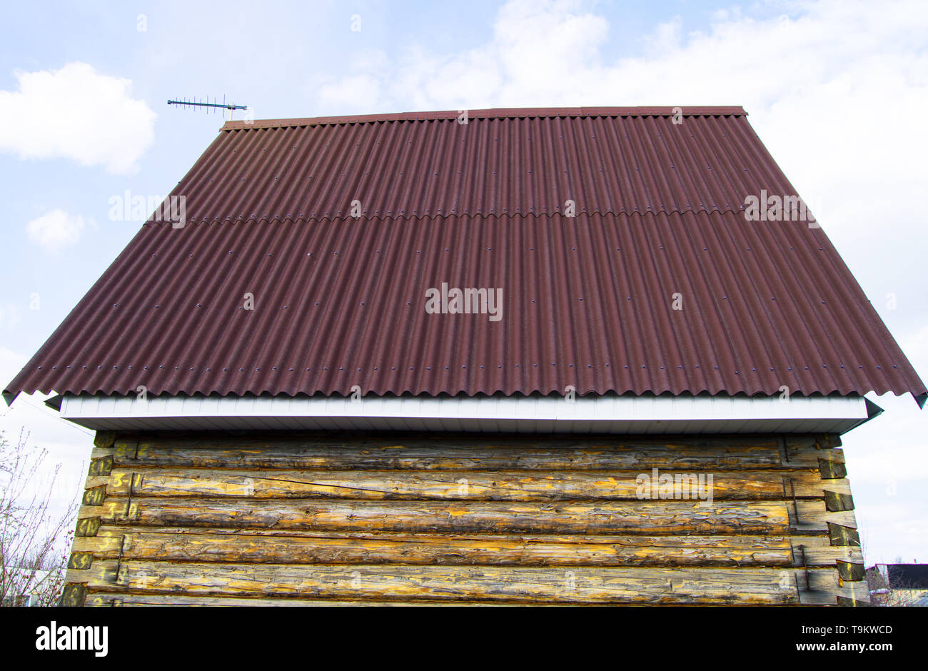 modern construction of the roof with red metal siding to a wooden house in the garden. Stock Photo