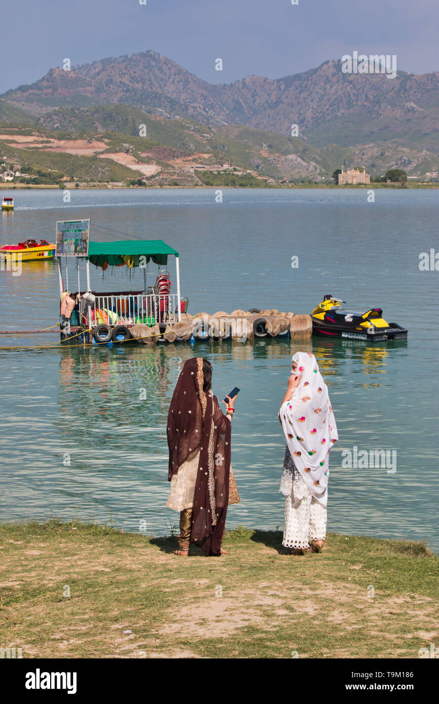 Khanpur, Pakistan - May 2019: Boat sailing in the lake with clouds in the backgroundTwo women standing by the lake in the afternoon Stock Photo
