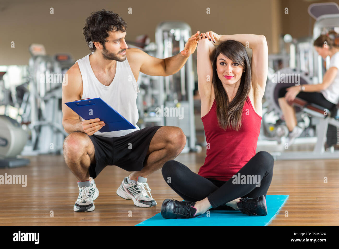 Woman doing stretching in a gym while a personal trainer watches her ...