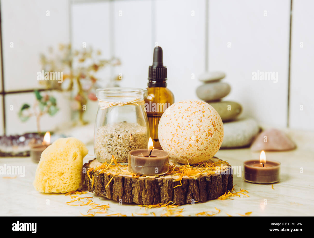 Side view of home wellness spa products, orange bath bomb, aroma bath salt, sea sponge, tea candles lit. Very zen set, tree of love and amethyst cryst Stock Photo