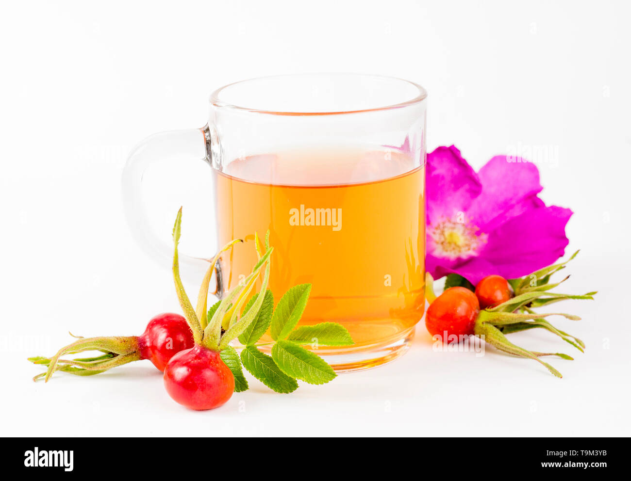 Side view of the rose hip or rosehip, also called rose haw and rose hep tea in clear glass cup, raw berries, blossom and leaves for decoration on whit Stock Photo