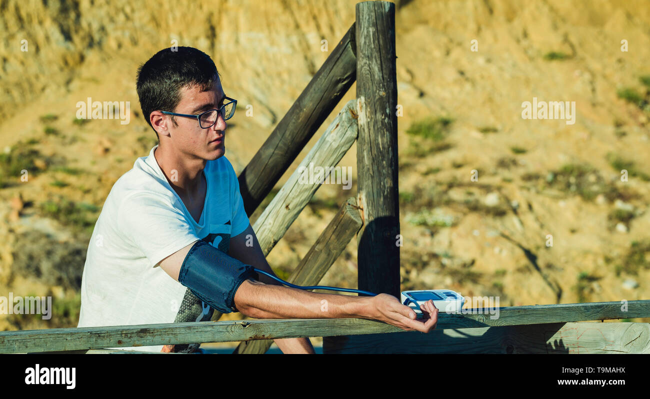 Hypertensive patient performing an automatic blood pressure test on the beach / man's self-control of blood pressure with a tensiometer on the outside Stock Photo