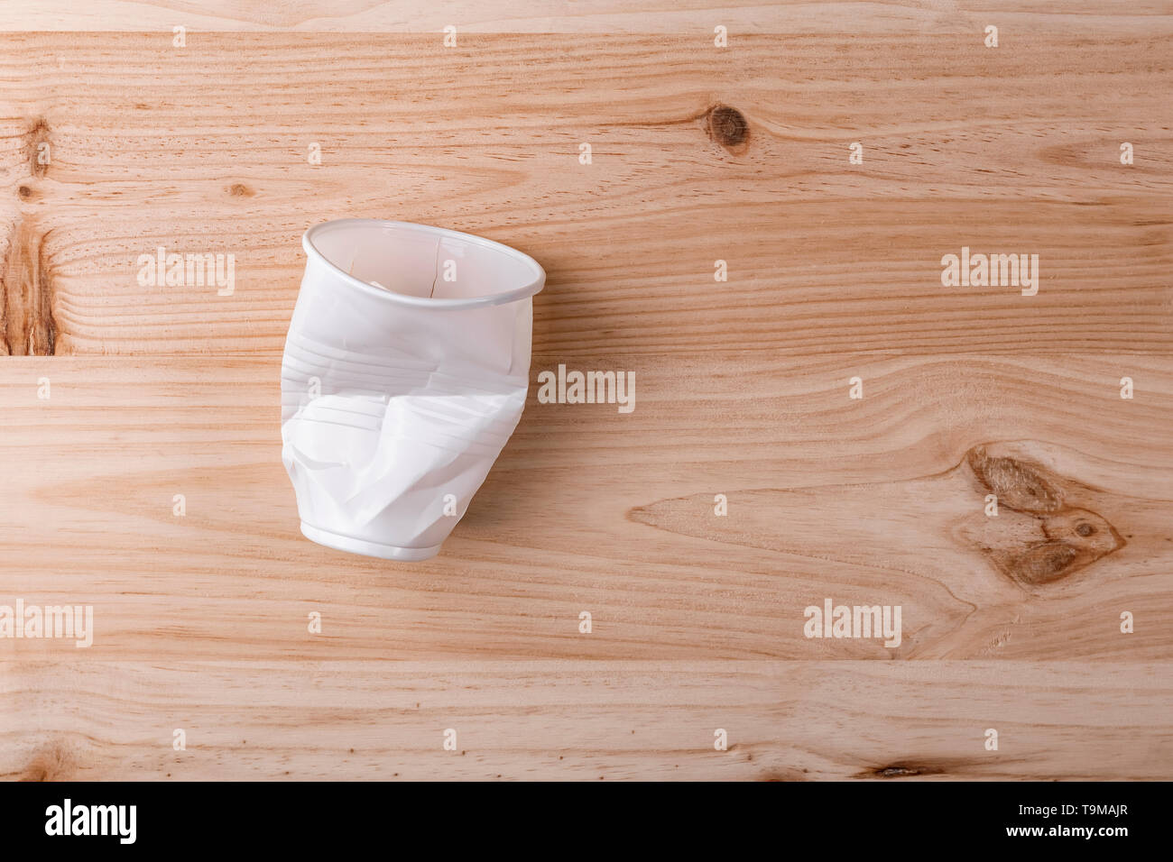 Broken crumpled white plastic Cup lies on a wooden table of natural ...