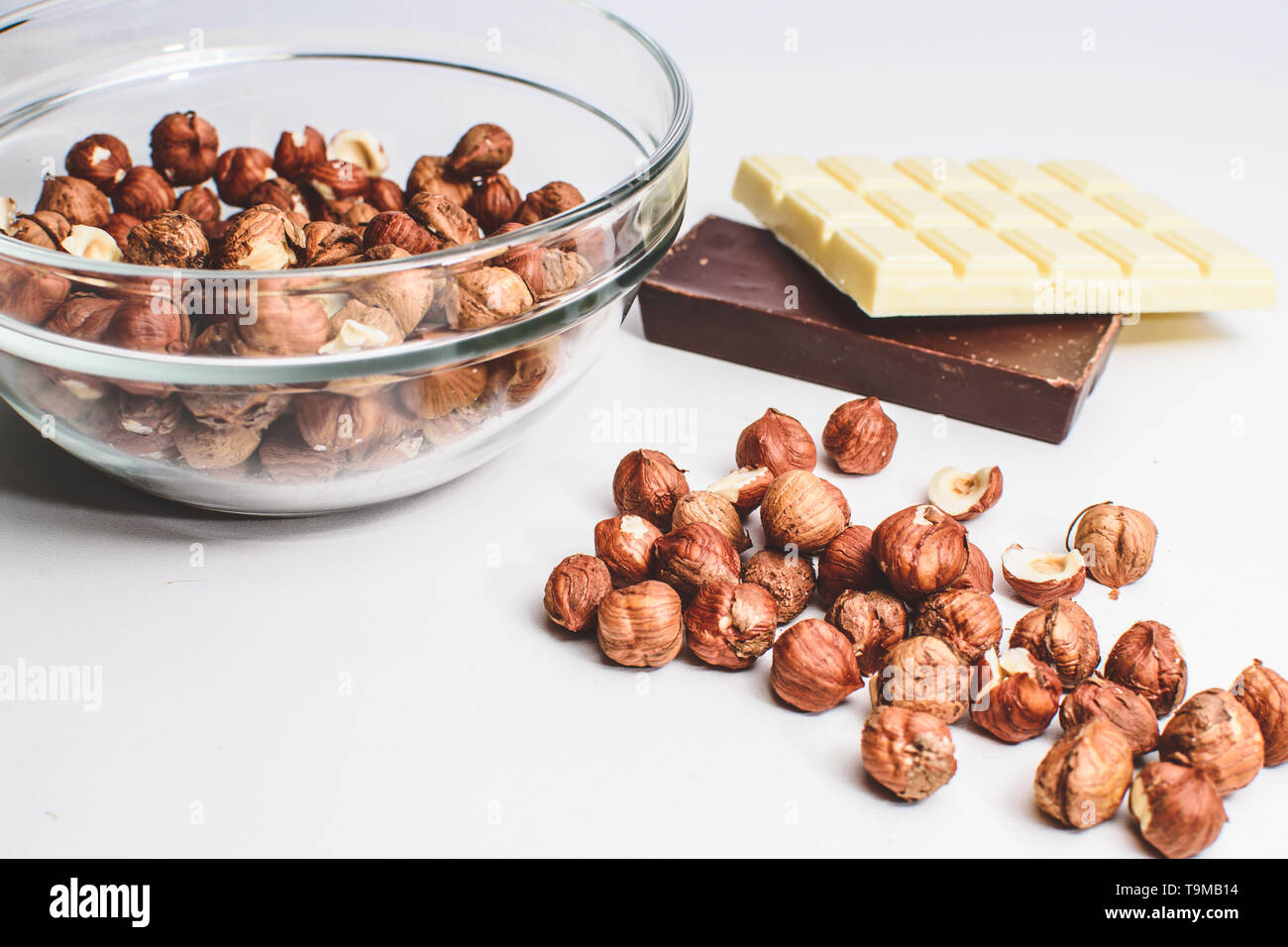 Isolated crystal bowl with hazelnuts, white chocolate and milk or dark chocolate against white background. Peeled nuts Stock Photo