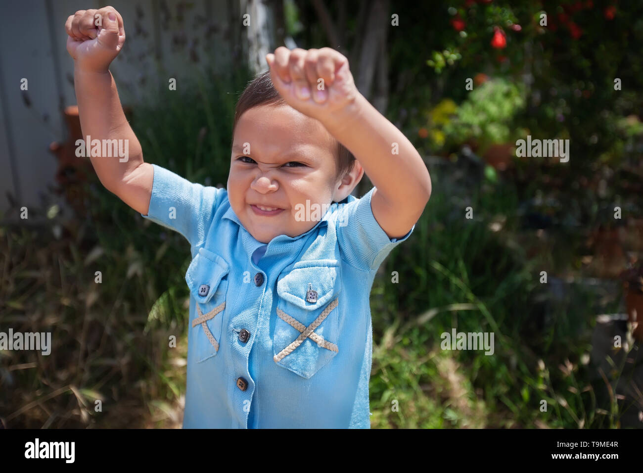 A 2 year old boy standing up by himself with arms up in the air and expressing joy. Stock Photo