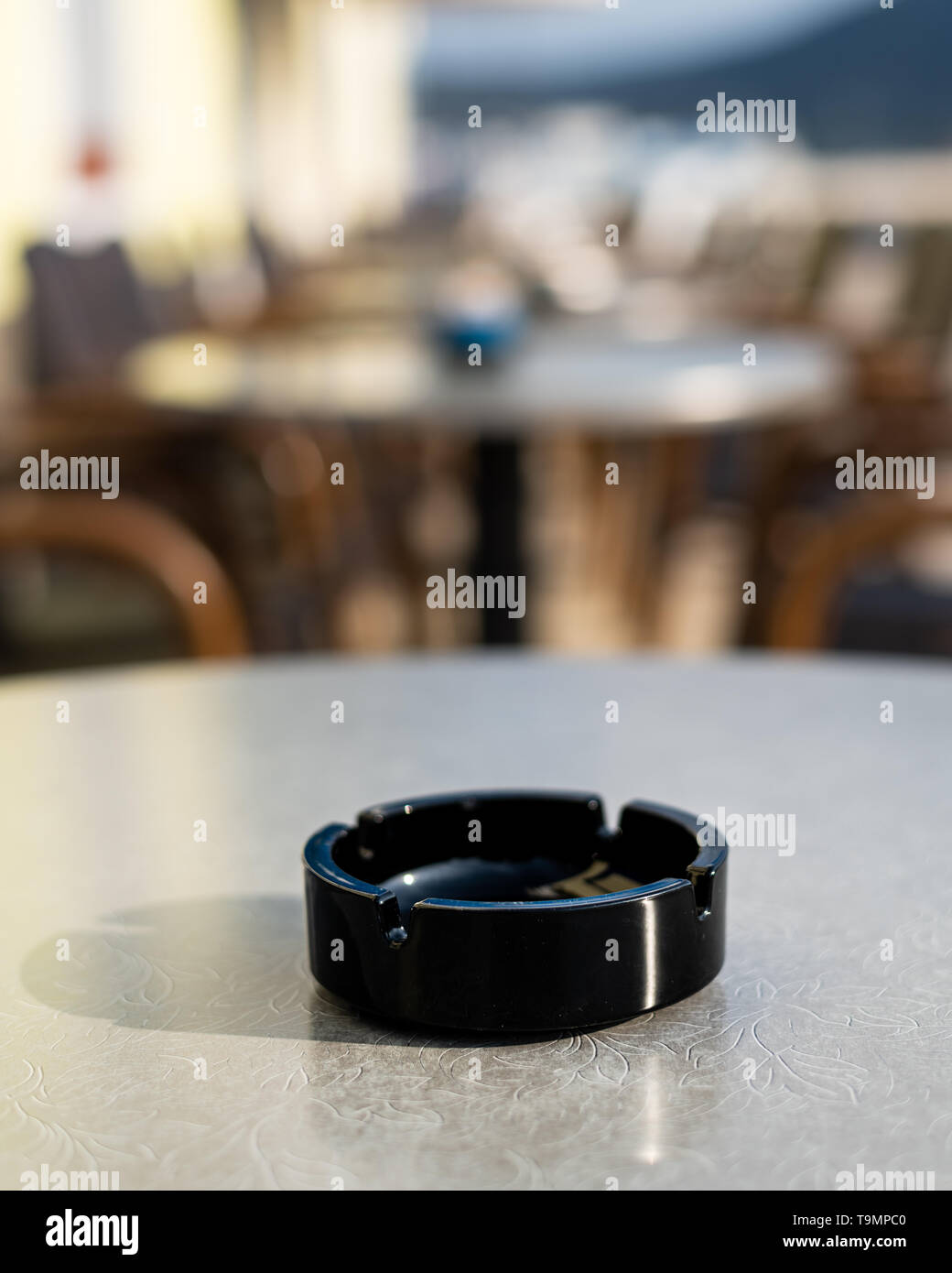 Closeup of a black ash tray on the table of a coffee shop, outside on a sunny day in spring Stock Photo