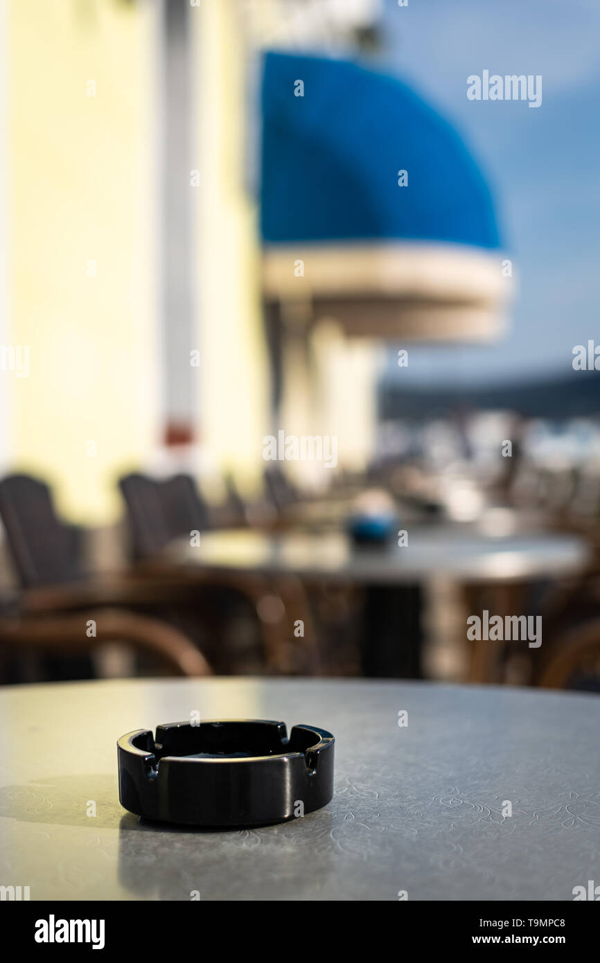 Closeup of a black ash tray on the table of a coffee shop, outside on a sunny day in spring Stock Photo
