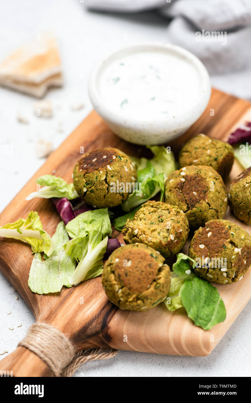 Falafel with yogurt sauce served on wooden cutting board. Closeup view, selective focus Stock Photo