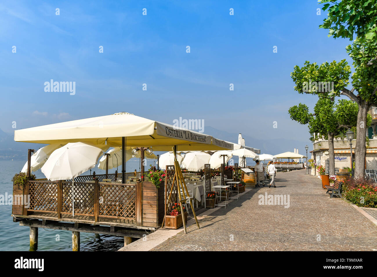 TORRI DEL BENACO, LAKE GARDA, ITALY - SEPTEMBER 2018: Outdoor dining area with sun canopy at a restaurant on the promenade on the edge of Lake Garda Stock Photo