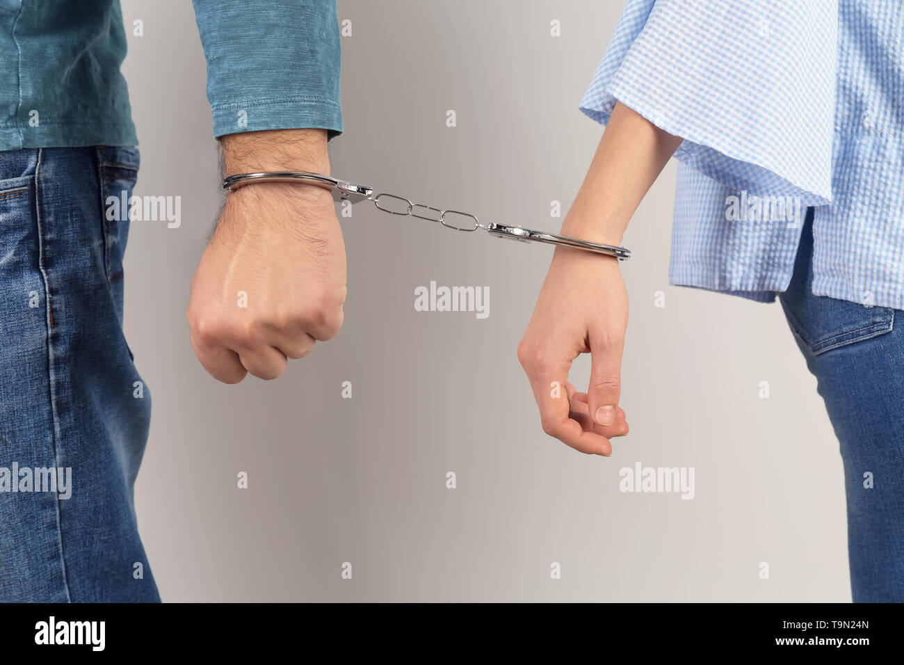 Couple with handcuffed together hands on light background. Concept of addiction Stock Photo