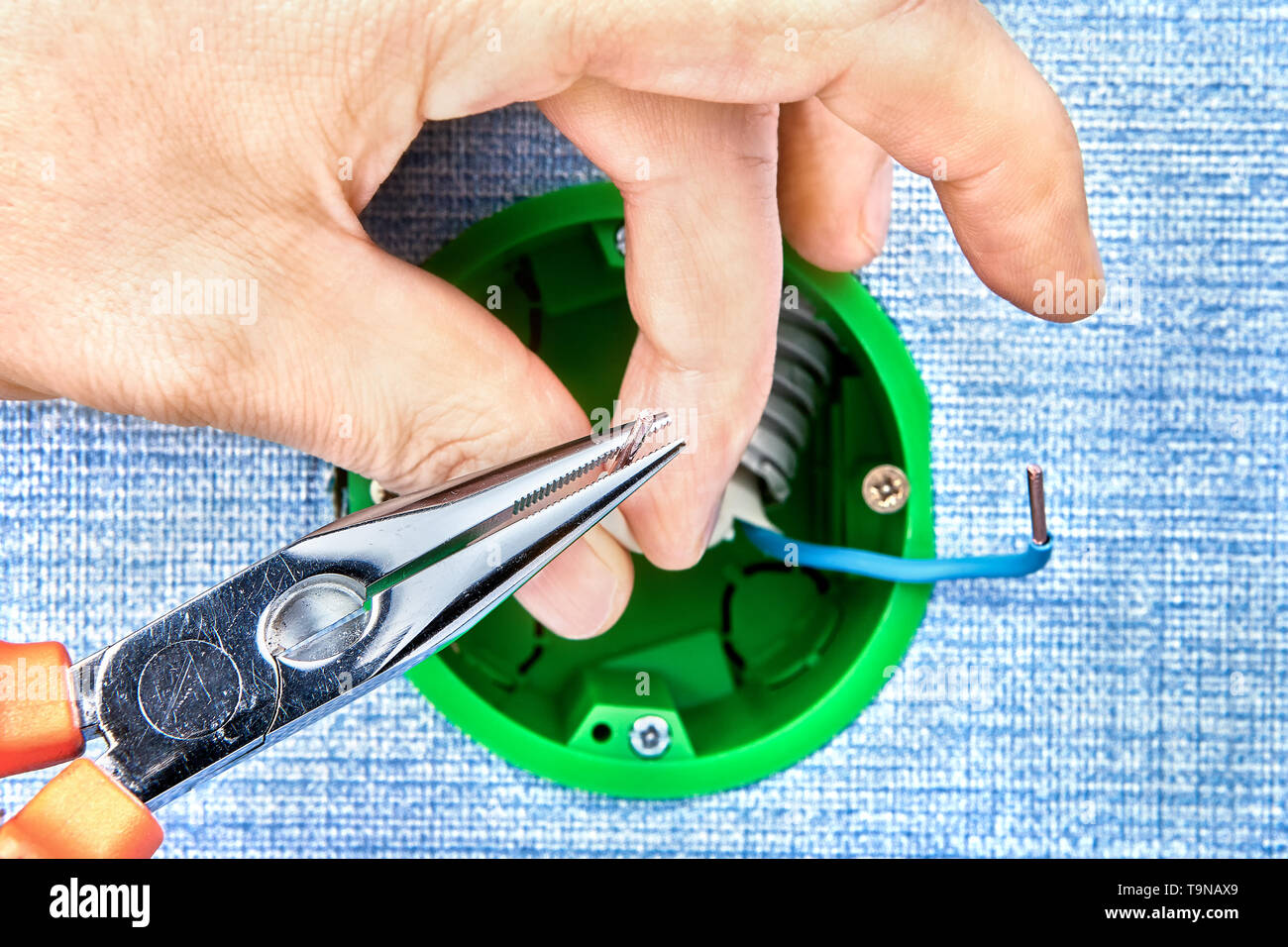Worker is cutting copper wires inside round electrical box with help of