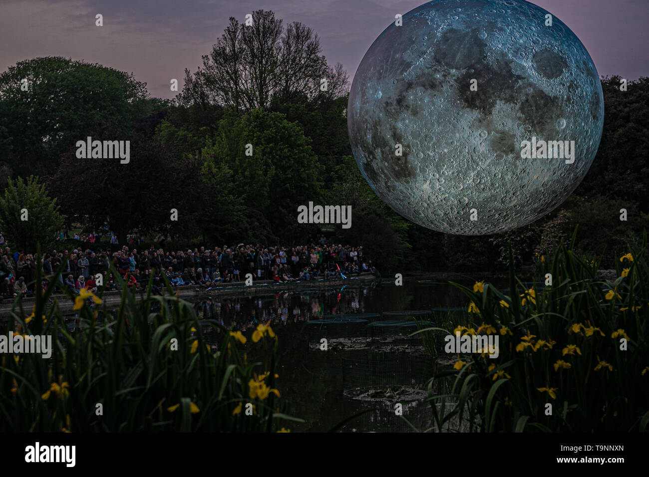 May 18, 2019 - Artist Luke Jerram's 7 metre diameter inflatable moon is suspended over the pond at Queens Park in Brighton during the Brighton Festival. The illuminated lunar model is one of several copies that tour the world for Luke's temporary exhibition. It features detailed NASA images of the moon's surface, with every centimetre of the lit sphere representing 5km of the moonâ€™s surface. The free arts event is part of the Brighton Festival, which is an annual celebration of art, music, theatre, dance, circus, and literature, which takes place in the city of Brighton and Hove during the m Stock Photo