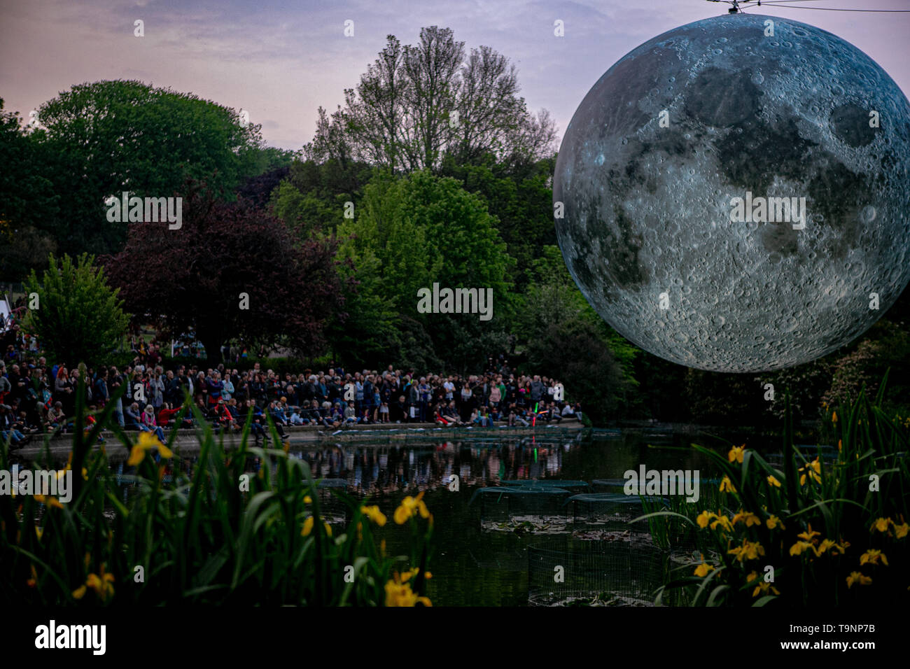 May 18, 2019 - Artist Luke Jerram's 7 metre diameter inflatable moon is suspended over the pond at Queens Park in Brighton during the Brighton Festival. The illuminated lunar model is one of several copies that tour the world for Luke's temporary exhibition. It features detailed NASA images of the moon's surface, with every centimetre of the lit sphere representing 5km of the moon's surface. The free arts event is part of the Brighton Festival, which is an annual celebration of art, music, theatre, dance, circus, and literature, which takes place in the city of Brighton and Hove during the m Stock Photo