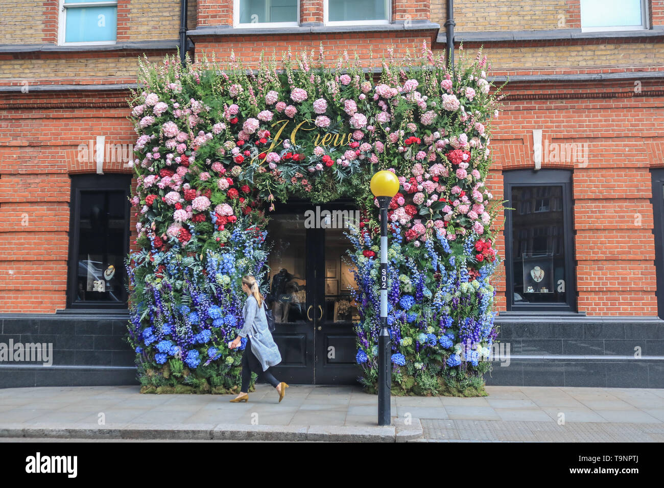 London, UK. 20th May, 2019. A pedestrian walks past a shop decorated with  flowers as shops retailers in fashionable Chelsea decorate their store  fronts with creative floral designs and displays to compete, image size:1300x956