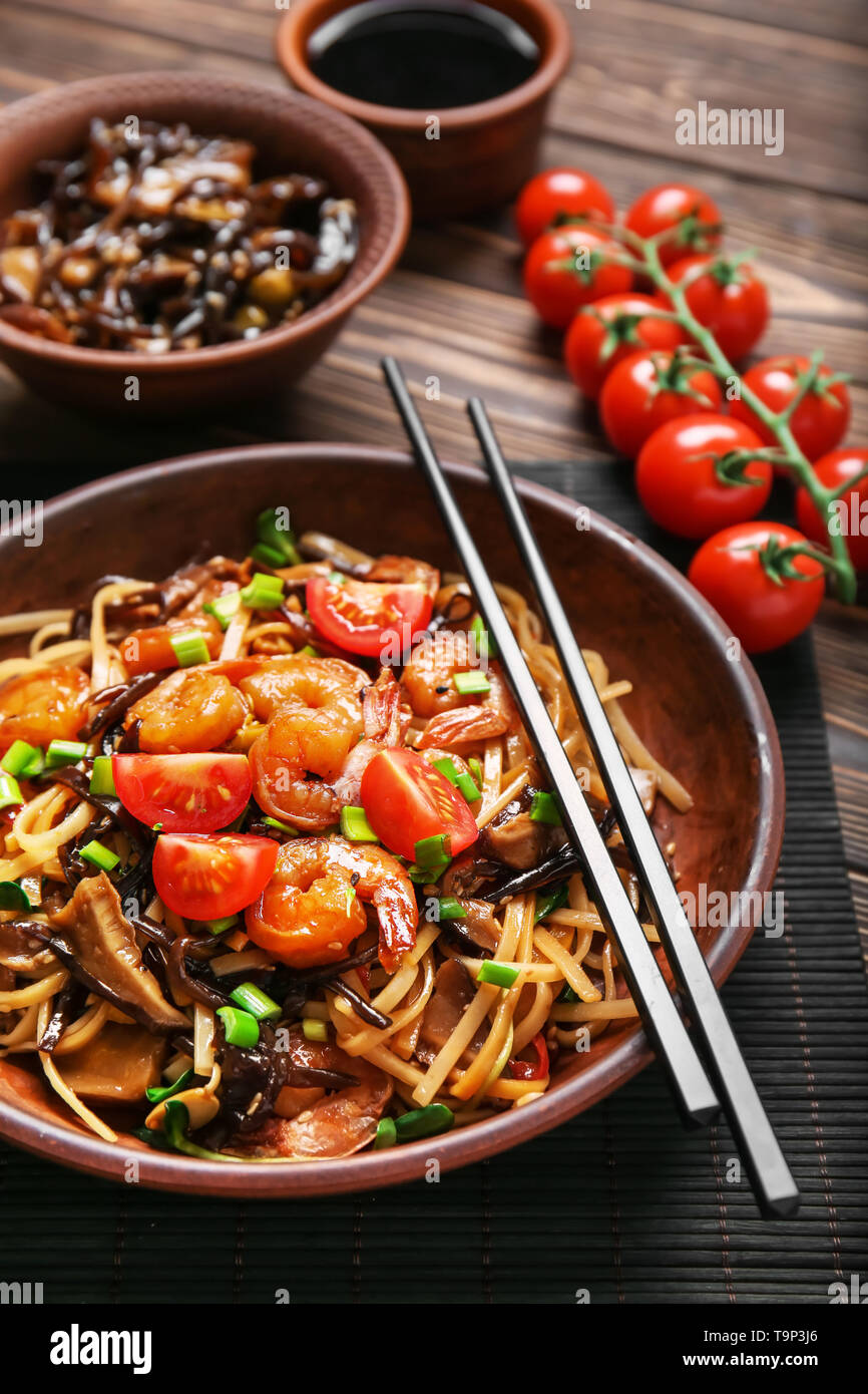 Plate with tasty chinese noodles, mushrooms and vegetables on wooden table, closeup Stock Photo