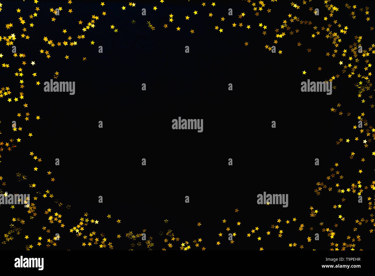 Star shaped golden sequins on a black background. Stock Photo