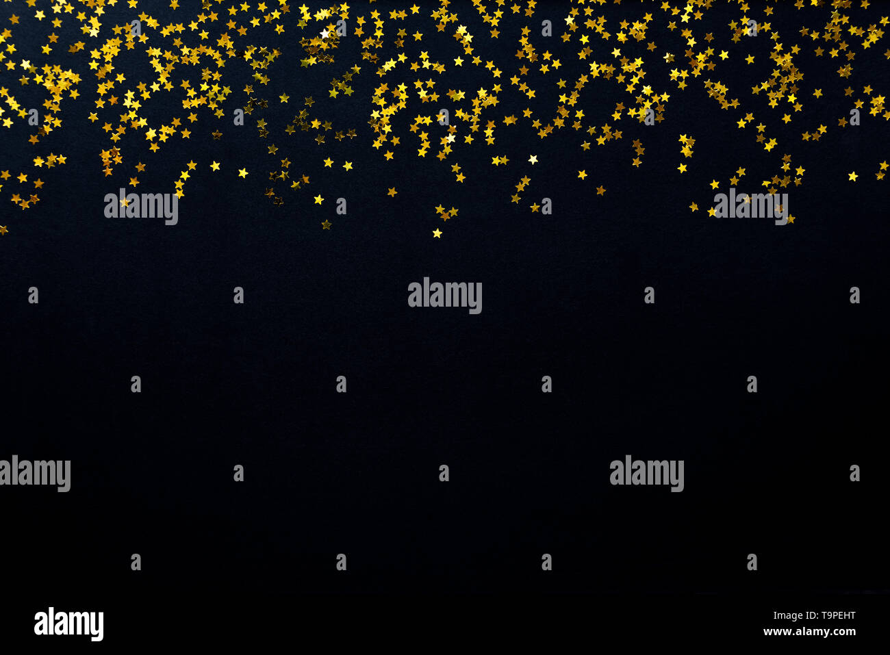Star shaped golden sequins on a black background. Stock Photo