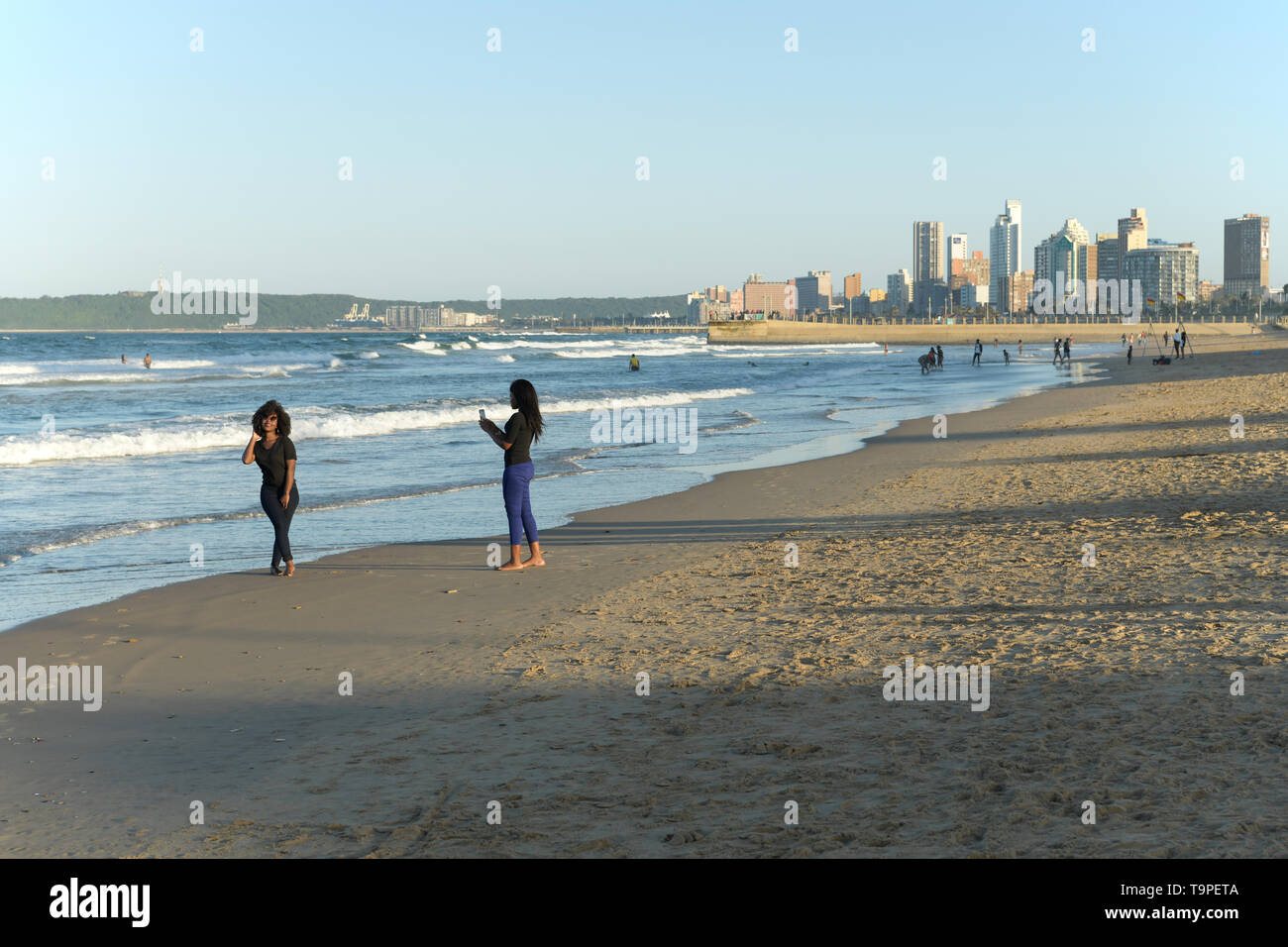 Posing for cell phone photo, two young adult women standing on beach, Durban, KwaZulu-Natal, South Africa, friends, landscape, skyline, city, ethnic Stock Photo