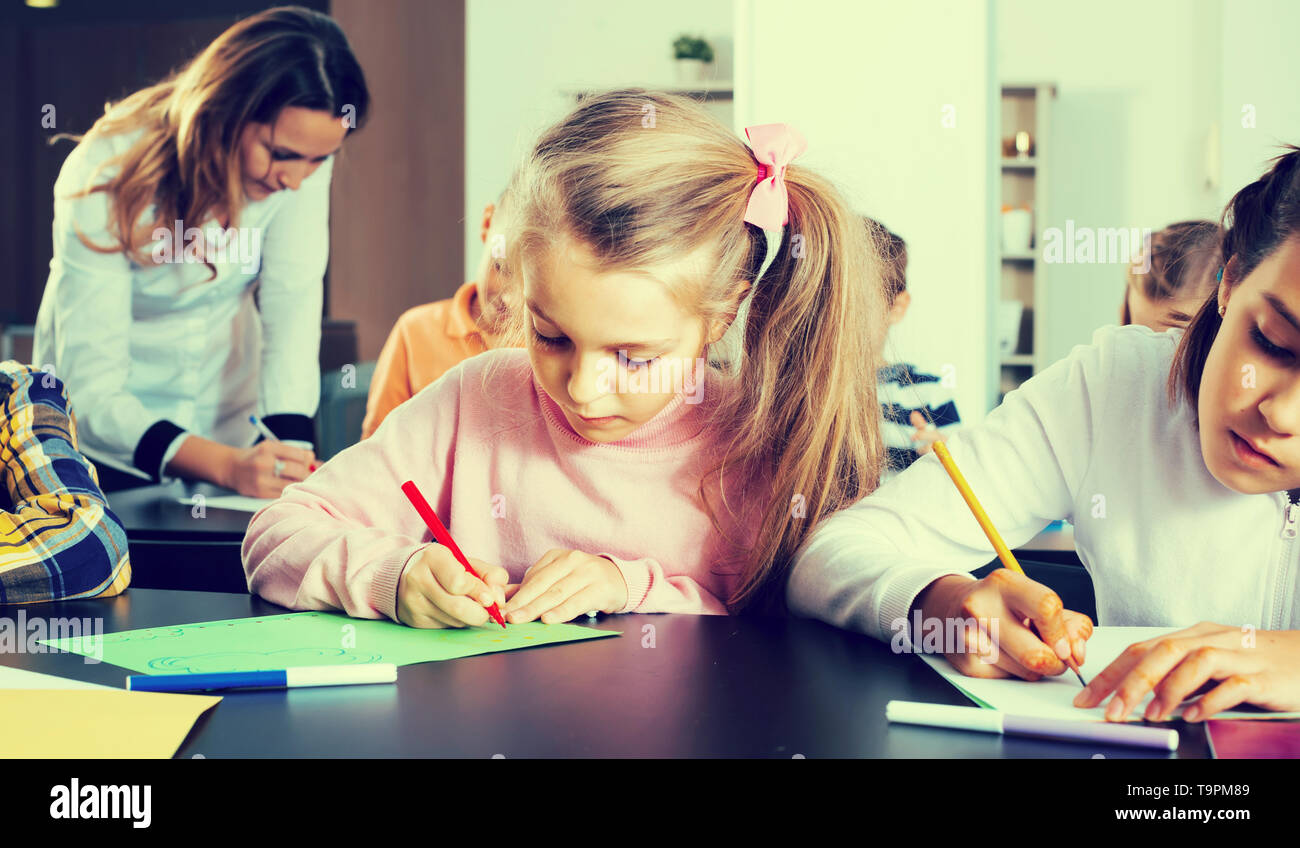 Portrait of girl and children in elementary age drawing at lesson in ...