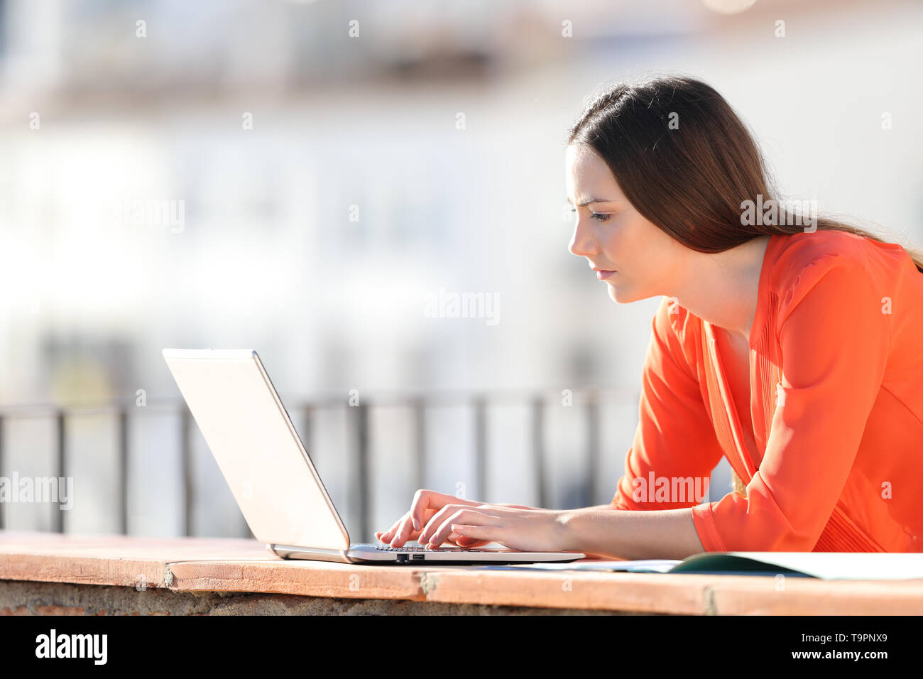 Side view portrait of a self employed writing on laptop in a balcony Stock Photo