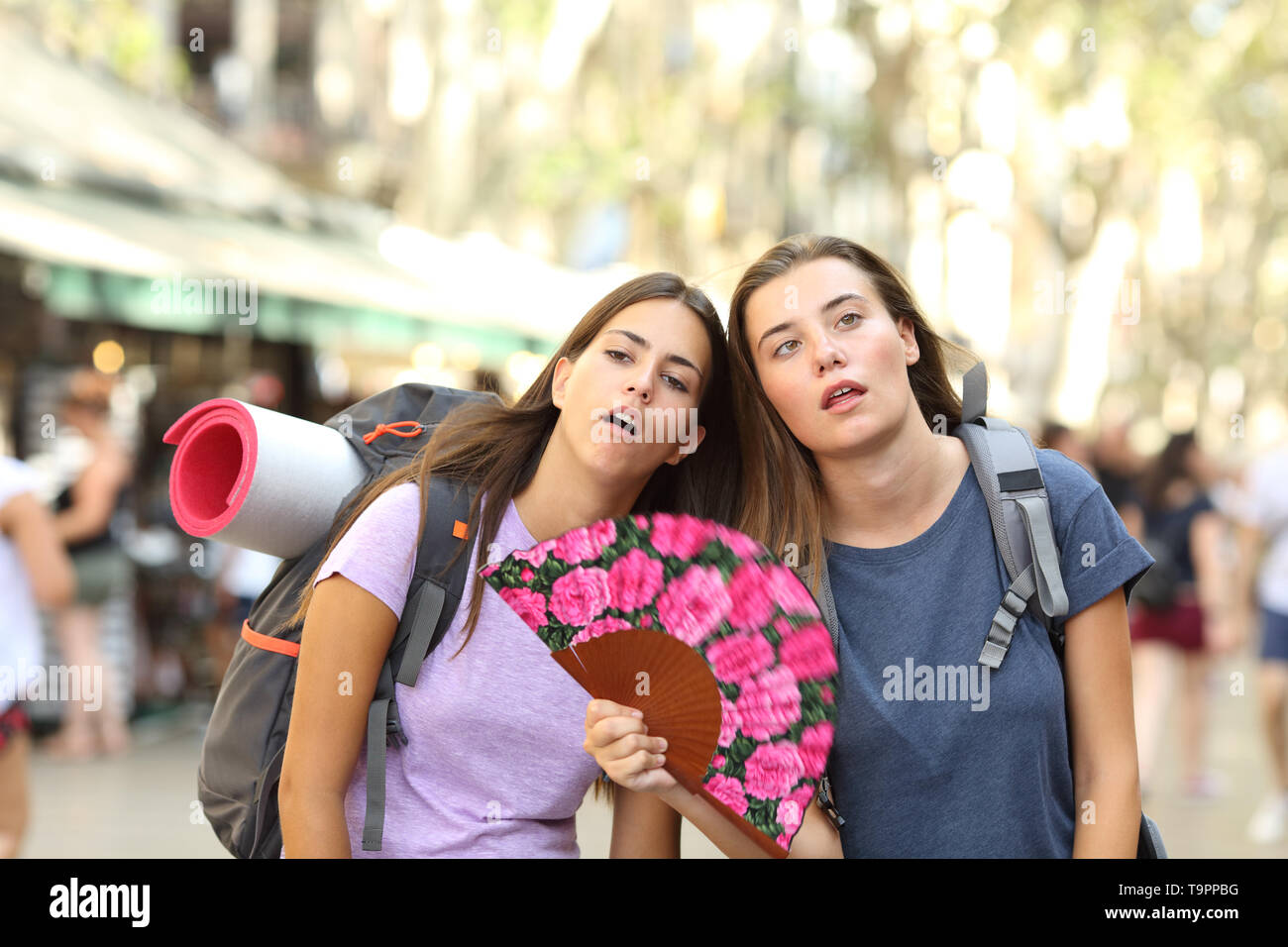 Two overwhelmed backpackers suffering heat stroke on summer vacation in the street Stock Photo