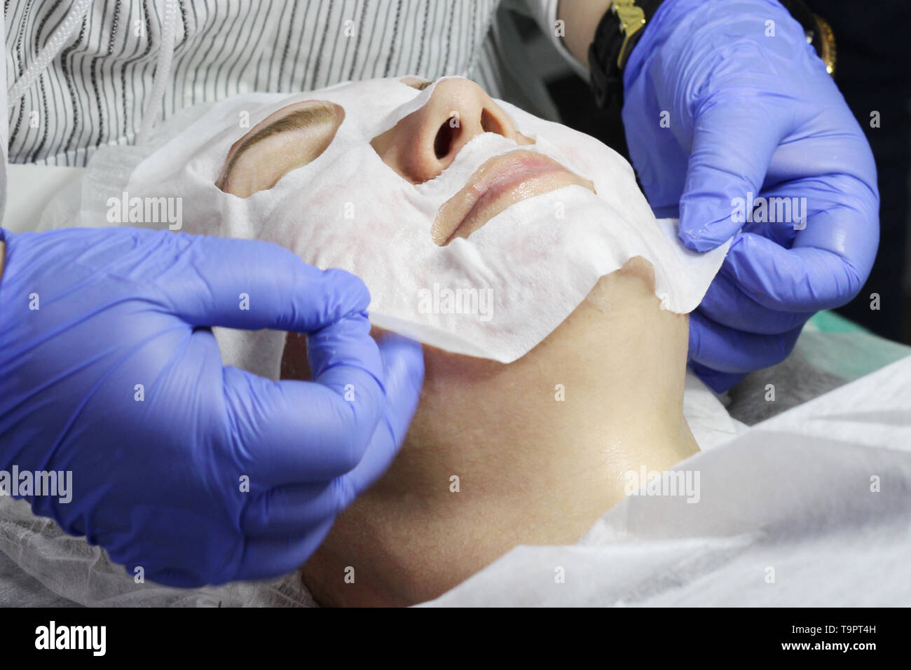 Moisturizing cosmetic mask for the woman. Hands in the gloves of a dermatologist, cosmetologist. Removing the mask from the face. The woman rejuvenate Stock Photo