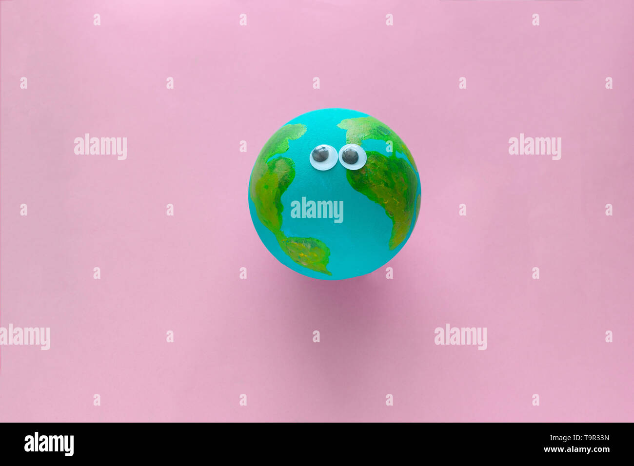 Earth planet model with googly eyes on a pastel pink background Stock Photo