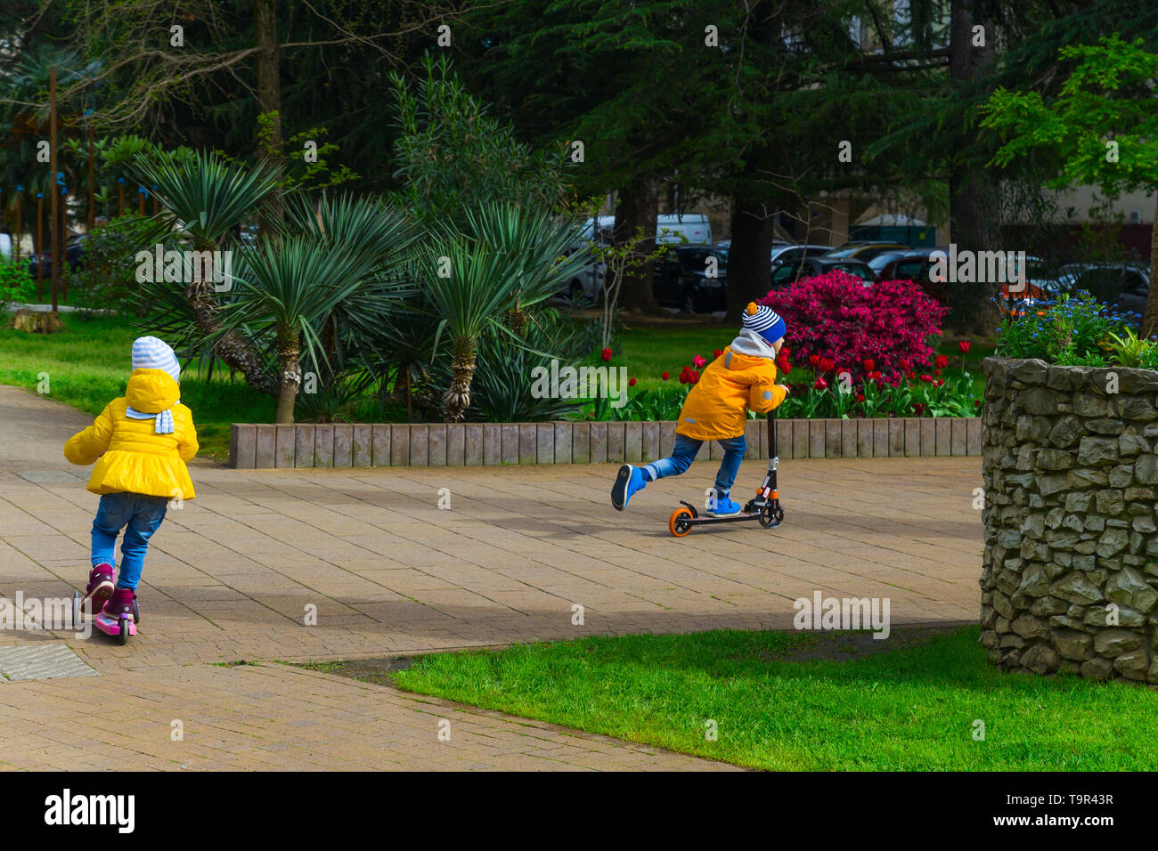 SOCHI,RUSSIA,  18 APRIL 2019 - boy and girl  in a bright yellow jackets riding   scooters in the park Stock Photo