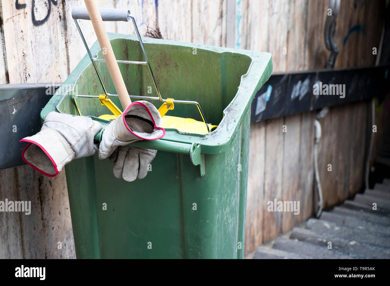Movable street cleaning garbage bin with broom in it and gloves on the handle, without worker; there is manual low payed workers deficiency Stock Photo