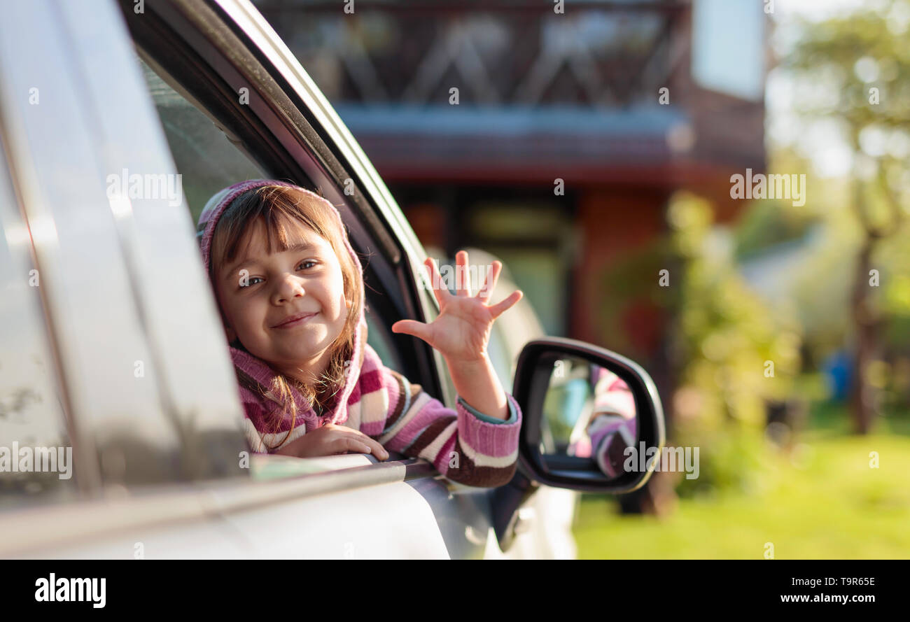 Pretty little girl in the car looking through car window and waving ...