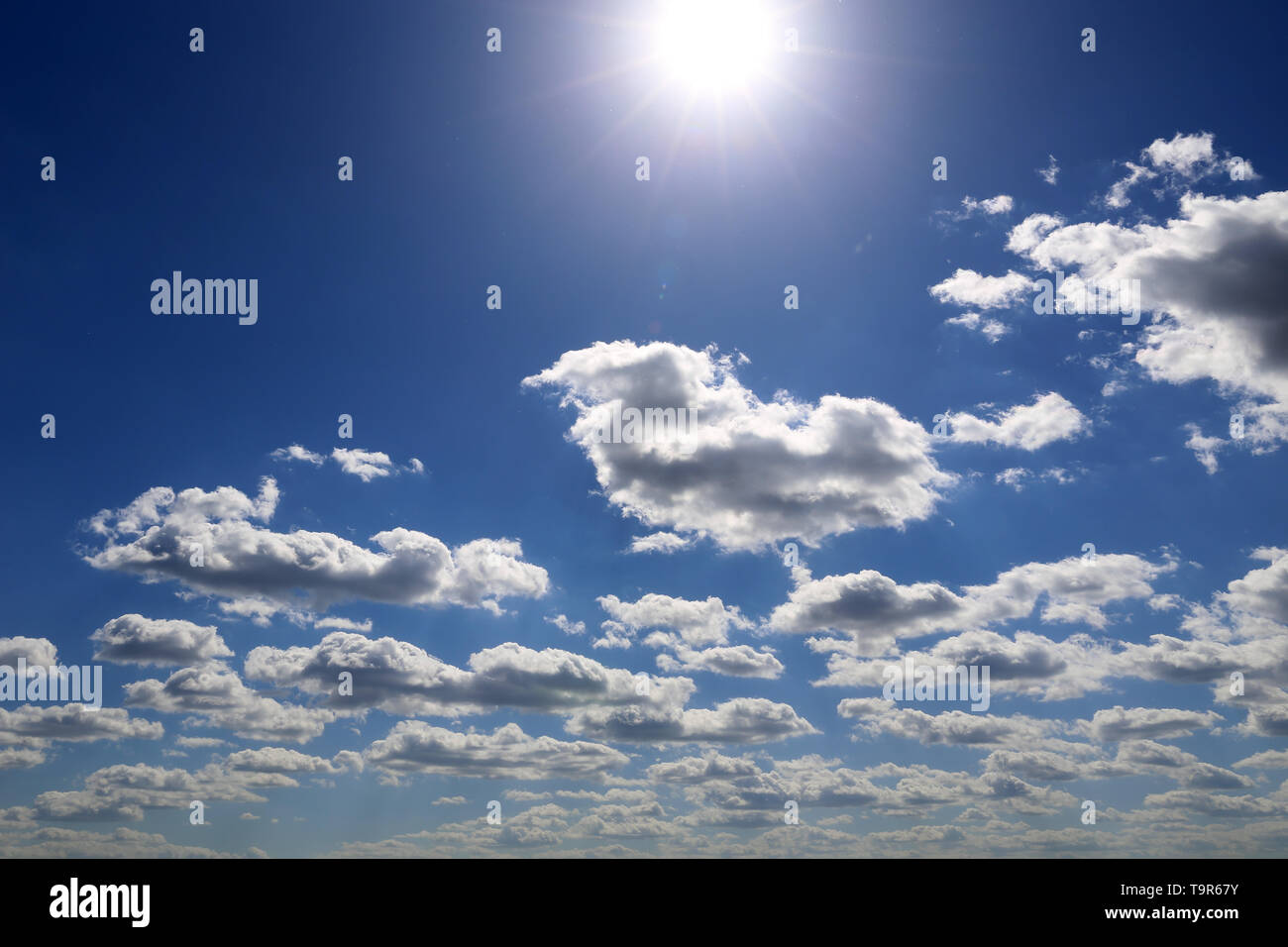 Shining sun and blue sky covered with white cumulus clouds. Summer cloudscape, beautiful background for good sunny weather Stock Photo