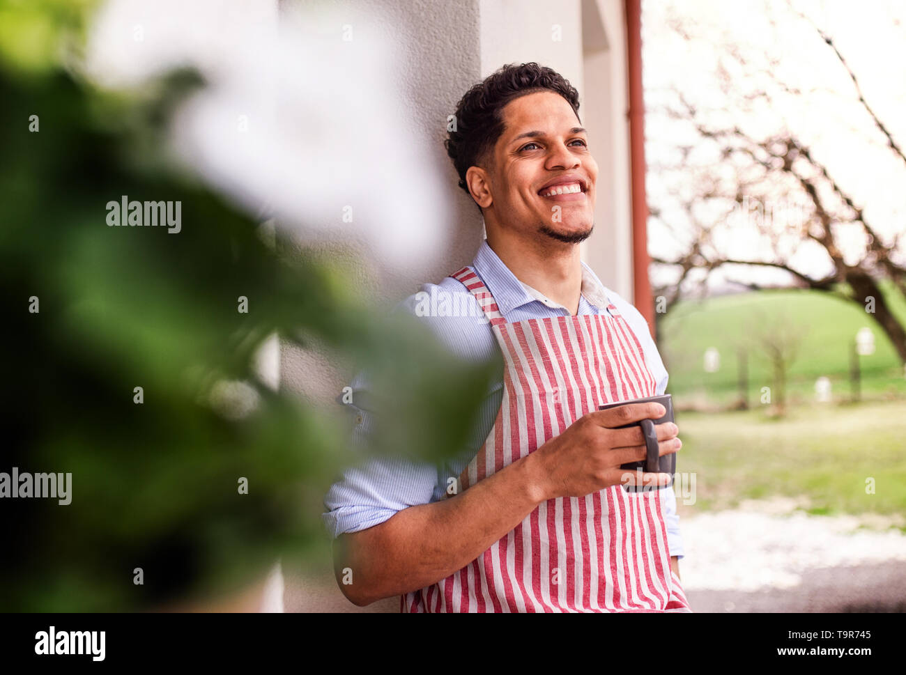 A portrait of young man gardener outdoors at home, holding a cup of coffee. Stock Photo