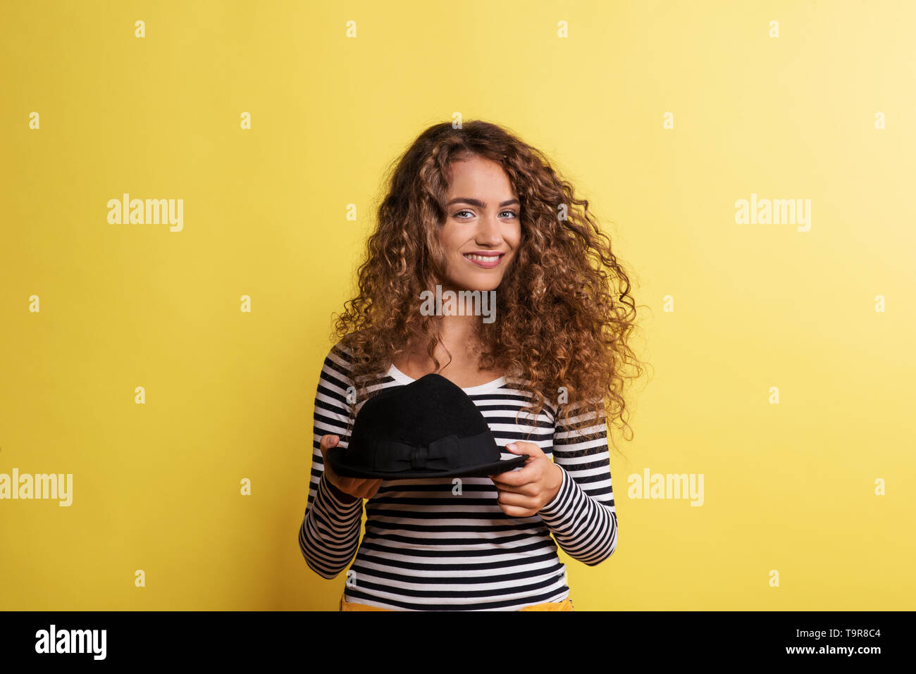 Portrait of a young woman with black hat in a studio on a yellow background. Stock Photo