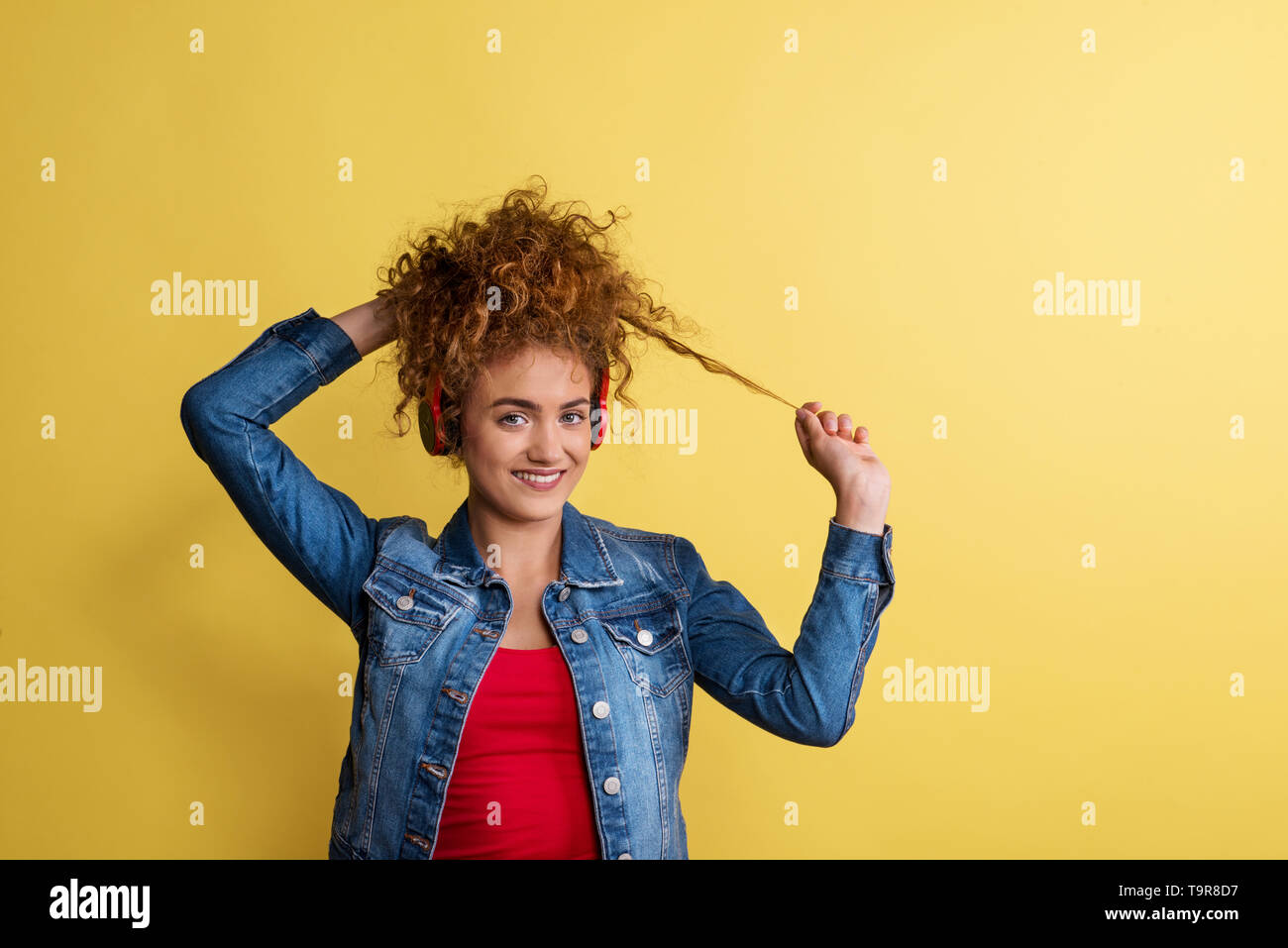 Portrait of a young woman with headphones in a studio on a yellow background. Stock Photo