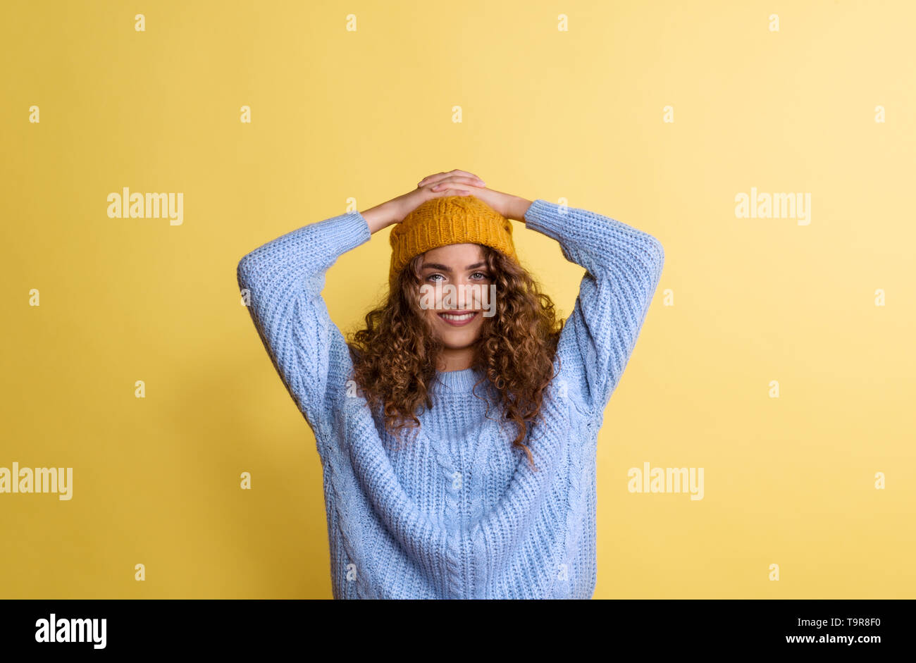 Portrait of a young woman with woolen hat in a studio on a yellow background. Stock Photo