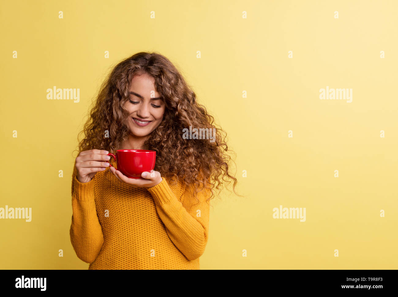 Portrait of a young woman with red cup in a studio on a yellow background. Stock Photo