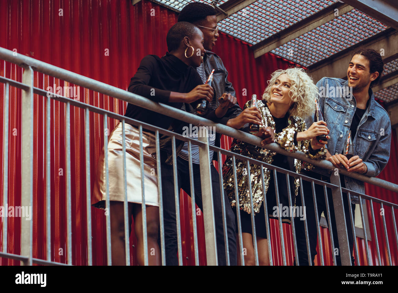 Multiethnic friends standing together at the railing with cola. Four