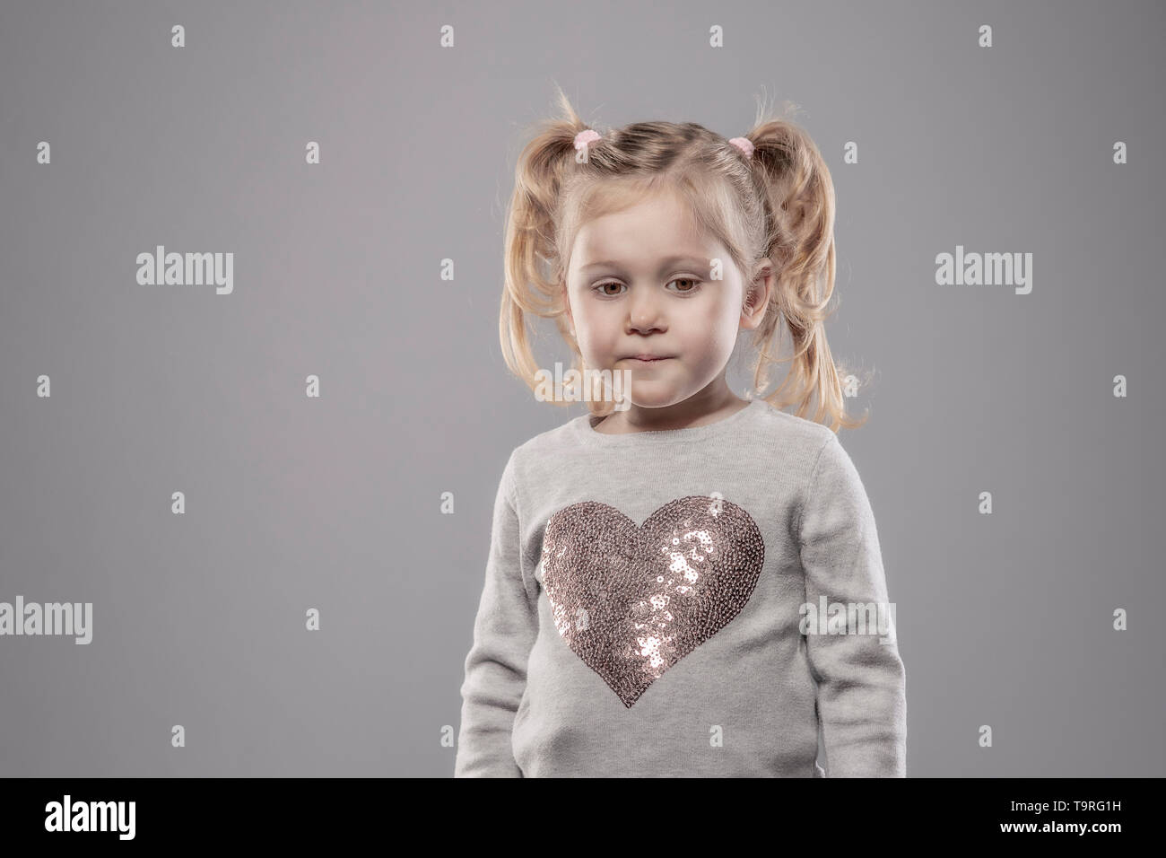 portrait of a pensive little girl of 3 years, blond hair with pigtails. Stock Photo