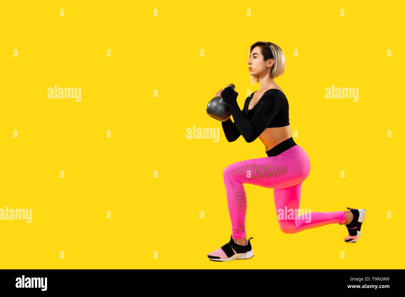 Fitness woman in fashionable pink and black sportswear work out with  kettlebell on yellow background. Strength and motivation Stock Photo - Alamy