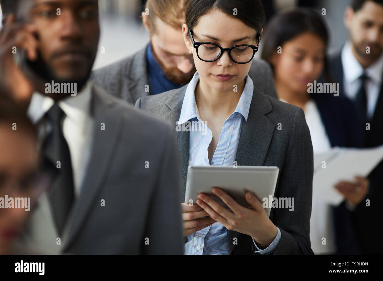 Busy lady reading document on tablet while standing in line Stock Photo