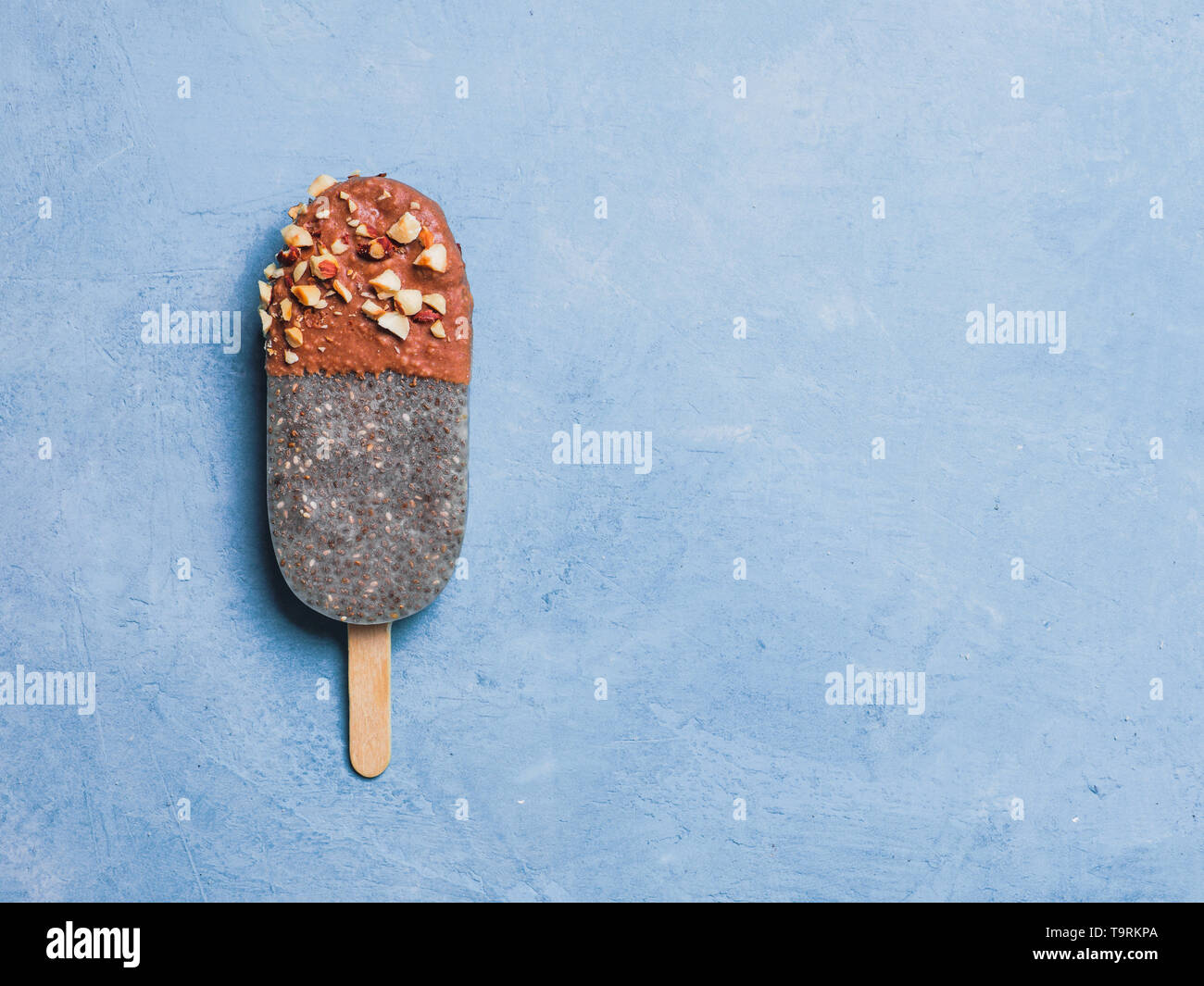Chia popsicle with chocolate and nuts on blue background. Healthy recipe and idea homemade vegan popsicle ice cream. Easter dessert idea. Copy space for text. Top view or flat-lay. Stock Photo