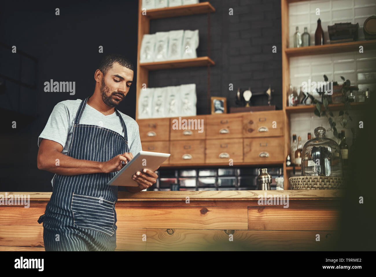 Young man in apron using digital tablet at his cafe Stock Photo