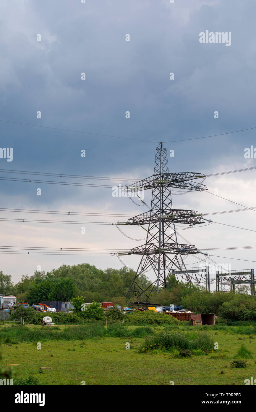 View across a field of a large electricity pylon, power lines and car scrapyard in Nursling, Test Valley, Southampton, Hampshire, southern England, UK Stock Photo