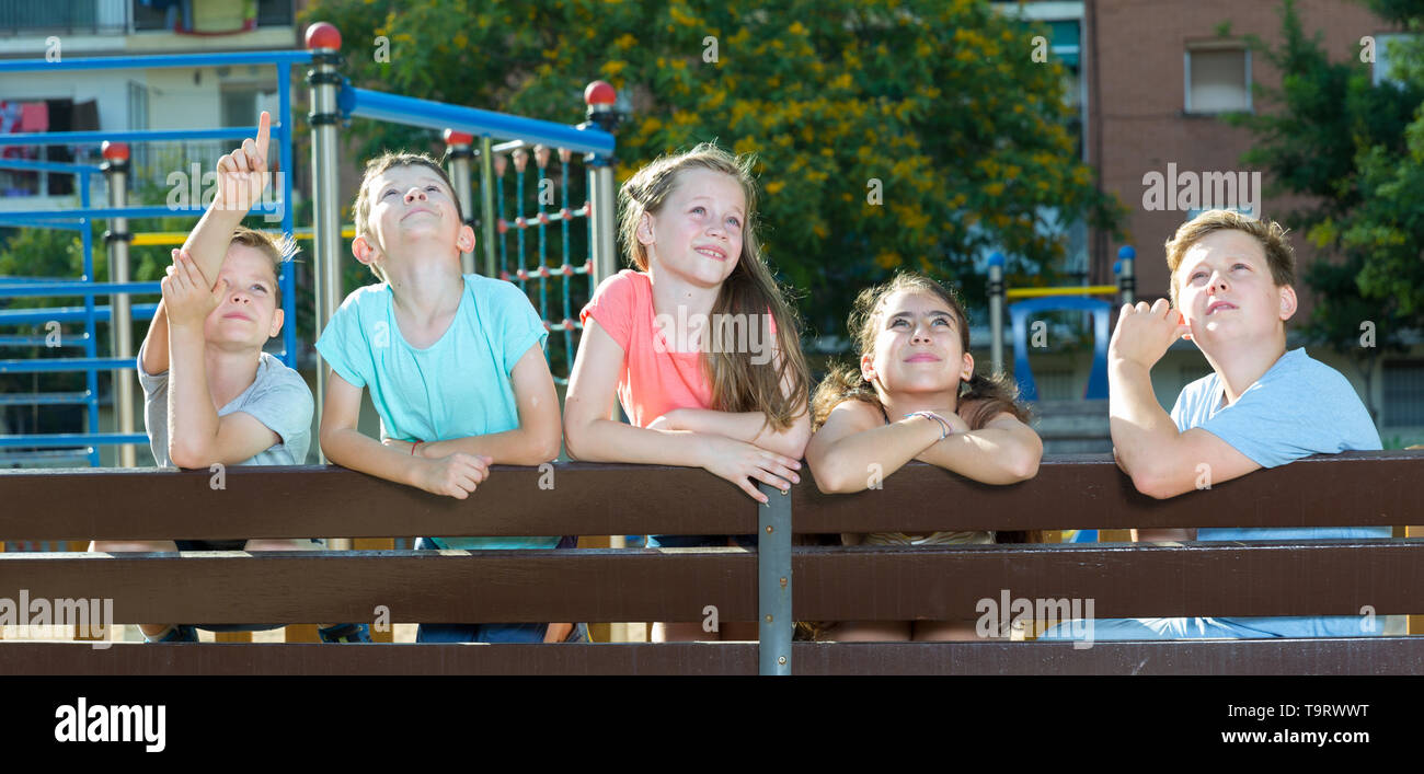 Five children sitting on a bench at the playground and point to ...