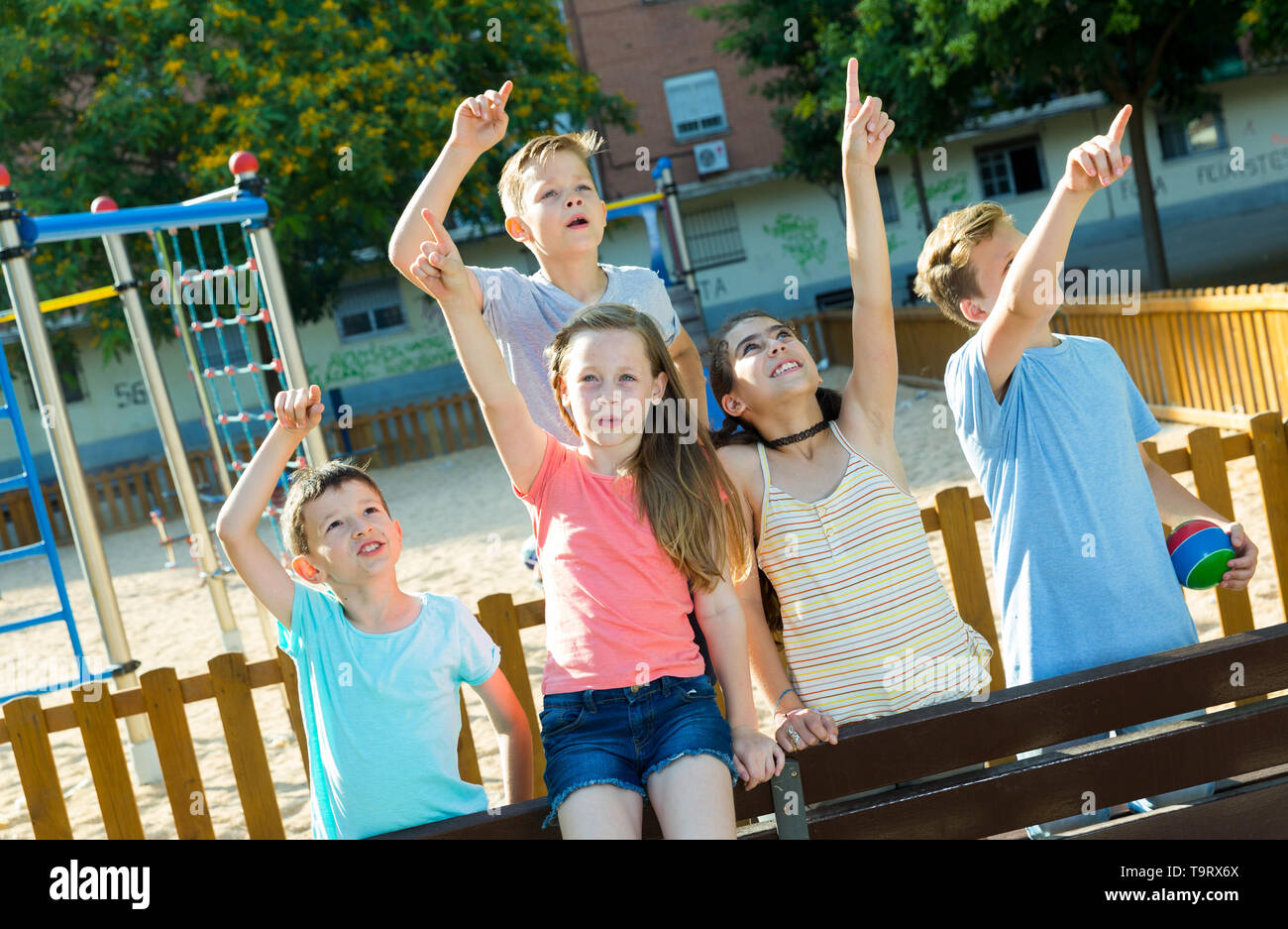 Five children sitting on a bench at the playground and point to ...